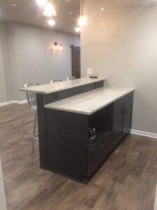 Modern kitchen with a two-tier island, marble countertops, wooden cabinets, and metal barstools on wooden flooring.