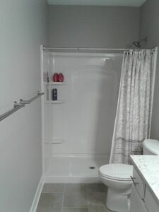 Bathroom with a walk-in shower, gray walls, shower curtain, towel bar, and a white toilet next to a granite countertop.