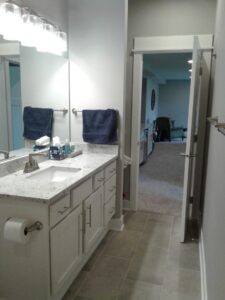 A bathroom with a sink, granite countertop, mirror, blue towels, and open door leading to a carpeted room with a chair.