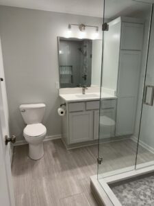 Modern bathroom with a toilet, vanity with sink and mirror, glass-enclosed shower, and light gray tile flooring.