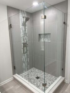 Glass-enclosed shower with gray tiles, mosaic accent, wall niche, and rainfall showerhead.