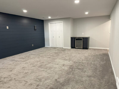 Carpeted room with gray walls, dark accent wall, recessed lighting, a small bar with a mini fridge, and double doors.