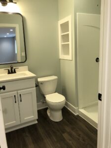 Small bathroom with a white toilet, sink, and mirror. Walk-in shower with glass door on the right. Walls are light green.