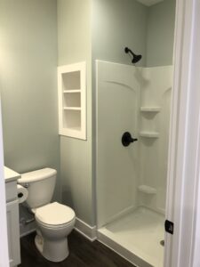 Simple bathroom with white toilet, corner shower unit, wall shelves, and light blue walls.