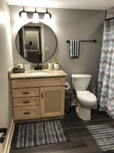 Modern bathroom with a round mirror, wooden vanity, toilet, striped towels, and a patterned shower curtain.