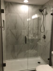 Glass shower enclosure with a wall-mounted showerhead, marble-patterned tiles, and sliding glass door.