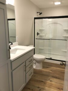Modern bathroom with a white vanity, glass-enclosed shower, and wooden floor.