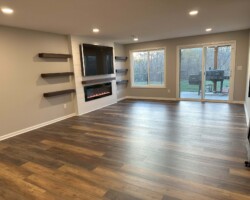 Spacious empty room with wood flooring, wall-mounted fireplace, shelves, and large sliding glass door leading outside.