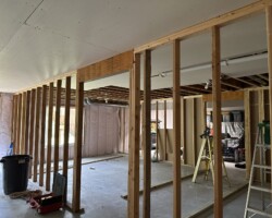 Wooden framing in a partially constructed room with a ladder and various tools scattered on the concrete floor.