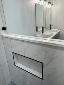 Bathroom with tiled shower wall niche, dual sinks, mirrors, and modern light fixtures.