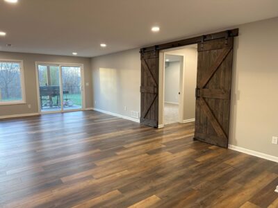 Spacious room with wooden floor, sliding barn doors, and a large window overlooking an outdoor area.